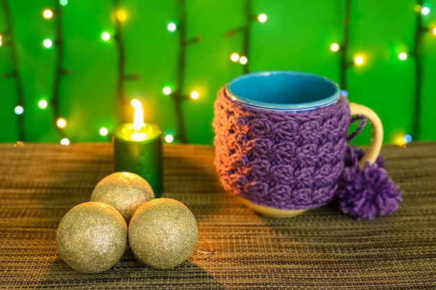 Vela acesa, caneca, bolas no fundo de uma guirlanda.