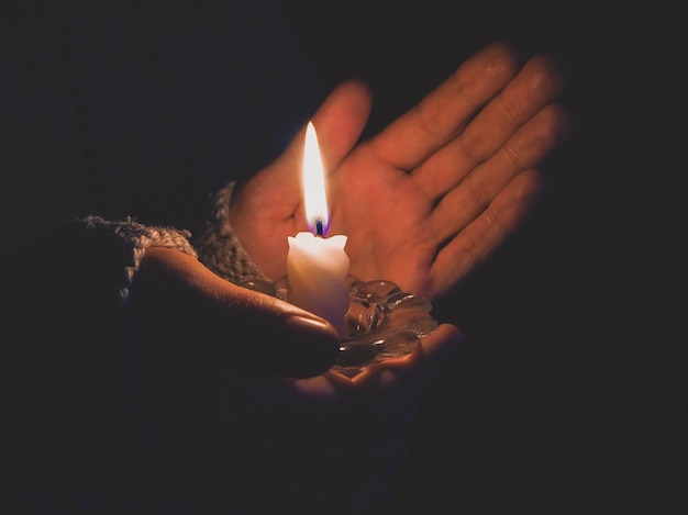 Vela acesa nas mãos femininas à noite.