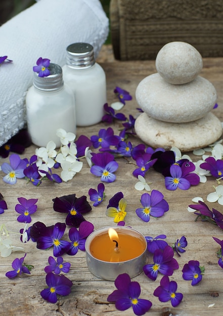 Vela acesa no meio de flores roxas de amor-perfeito e um conjunto de spa com loção para a pele