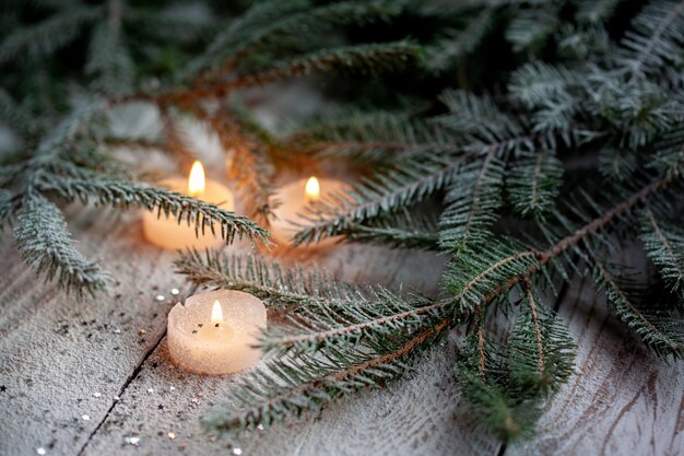 Vela ardiente y decoración de Navidad sobre nieve con ramas de pino sobre fondo blanco de madera.