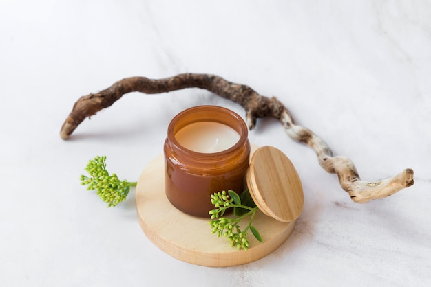 Vela aromática en podio de madera con palo y ramitas verdes.