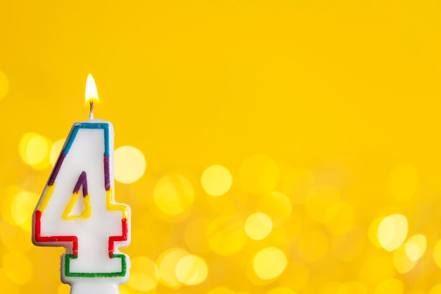 Vela de celebración de cumpleaños número 4 contra luces brillantes y fondo amarillo