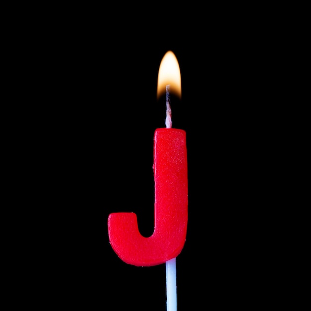 Vela de cumpleaños de la celebración de la letra J contra un fondo negro