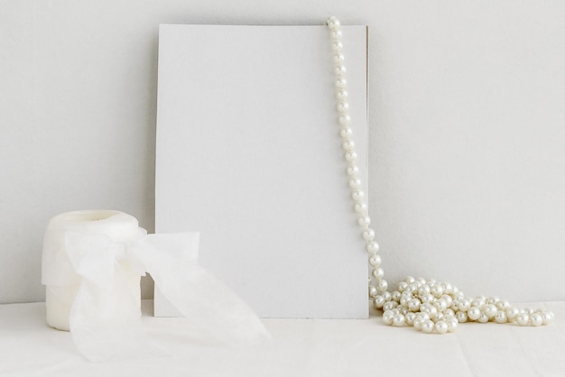 Vela de cartão branco em branco e colar de pérolas sobre fundo branco Fundo romântico para o convite
