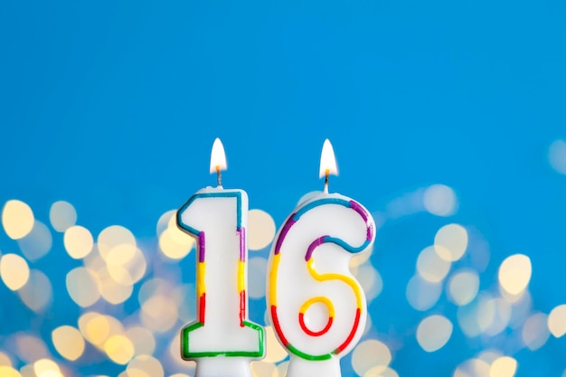 Vela de comemoração de aniversário número 16 contra luzes brilhantes e fundo azul