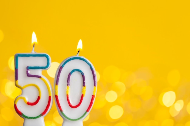 Vela de comemoração de aniversário número 50 contra luzes brilhantes e fundo amarelo