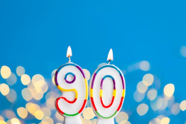 Vela de comemoração de aniversário número 90 contra luzes brilhantes e fundo azul