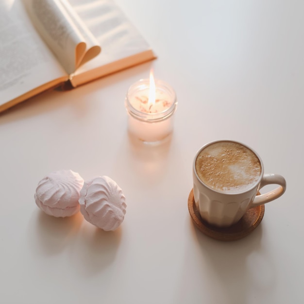 Vela de flor de xícara de café e um livro sobre uma mesa branca, vista superior, decoração mínima de interiores para casa