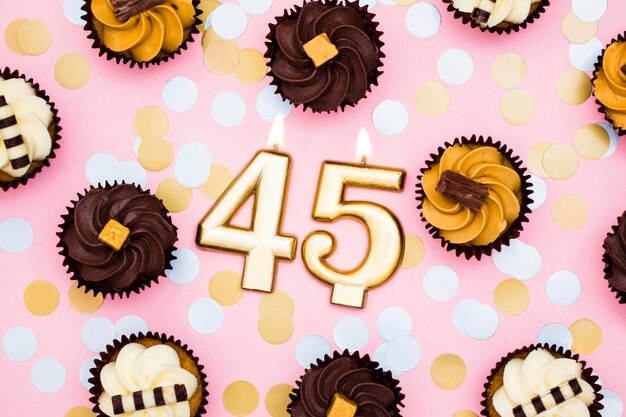 Foto vela de ouro número 45 com cupcakes contra um fundo rosa pastel