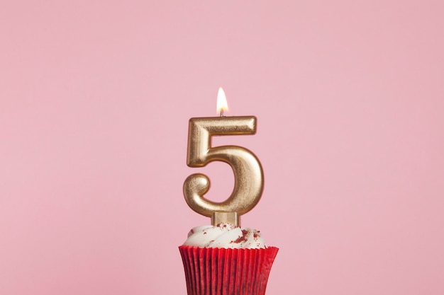 Vela de ouro número 5 em um cupcake contra um fundo rosa pastel