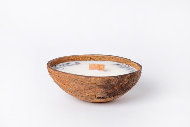 Vela decorativa de cera de soja natural en una cáscara de coco con mecha de vela de madera sobre una superficie blanca brillante
