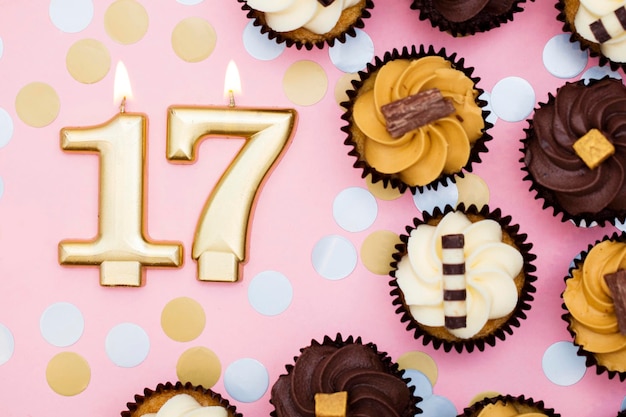Vela dorada número 17 con cupcakes sobre un fondo rosa pastel