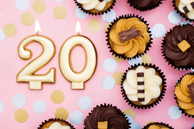 Vela dorada número 20 con cupcakes sobre un fondo rosa pastel