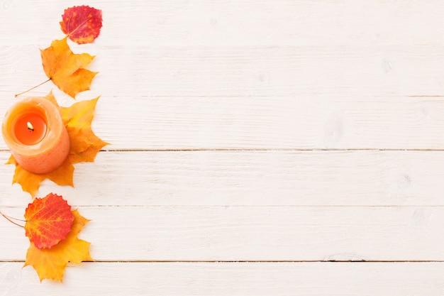 Vela con hojas de otoño en la pared de madera blanca