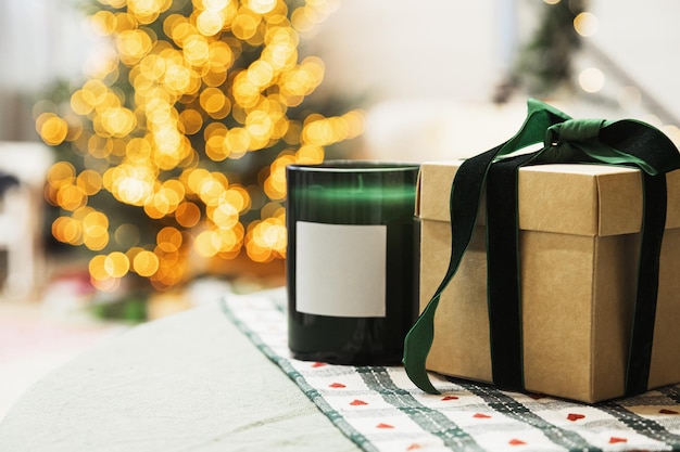 Vela perfumada y caja de regalo con cinta decorada árbol de navidad con luces en bokeh en el fondo