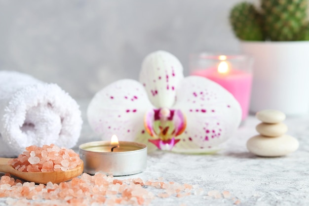 Vela perfumada de sal rosa do Himalaia, flor de orquídea, pedras zen e toalha, conceito de spa de beleza relaxante
