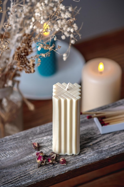 Una vela rectangular hecha a mano sobre un soporte de madera con el telón de fondo de otras velas encendidas en la parte trasera Ambiente acogedor