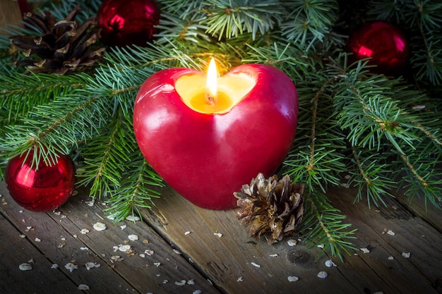 Vela roja ardiente con ramas de árbol de Navidad y conos de pino en un fondo de madera