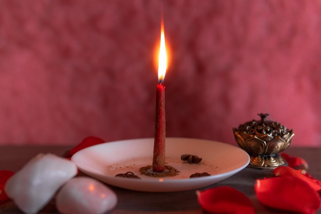 Una vela roja encendida sobre un fondo rosa preparada con canela molida con incienso y cuarzo rosa copiar pegar Halloween creencias espirituales magia blanca