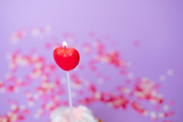 Vela roja en forma de un primer plano del corazón sobre un fondo púrpura Concepto de día de San Valentín y cumpleaños