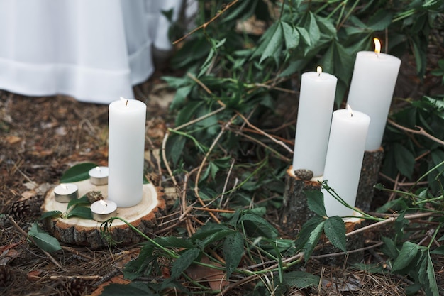 Foto velas acesas em suportes feitos de cortes de árvores no chão em decoração de casamento com folhagem verde