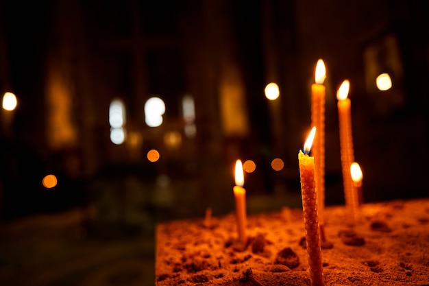 Velas acesas em uma igreja em um fundo escuro. Velas memoráveis. Velas Acesas No Templo, Fogo Sagrado. Velas acesas na igreja escura.