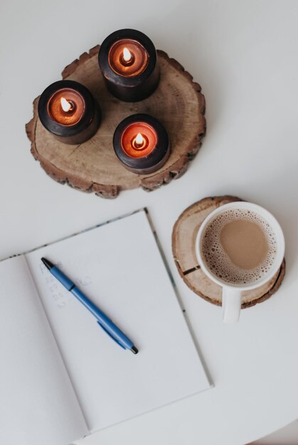 velas acesas um caderno de trabalho uma xícara de café bloco de notas uma caneta fogo vela