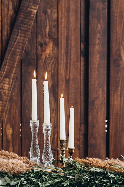 Velas altas brancas em castiçais de cristal no fundo texturizado de madeira rústico.