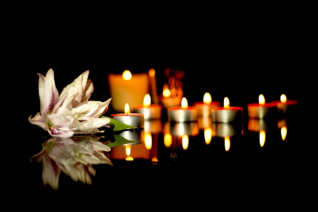 Velas blancas de lirio de un funeral en una placa con el reflejo de las luces de fondo de luto