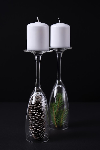 Velas blancas en las patas de una copa de champán con una piña y ramas de abeto sobre un fondo negro. El concepto de candelabros en el interior para el nuevo año. Foto vertical