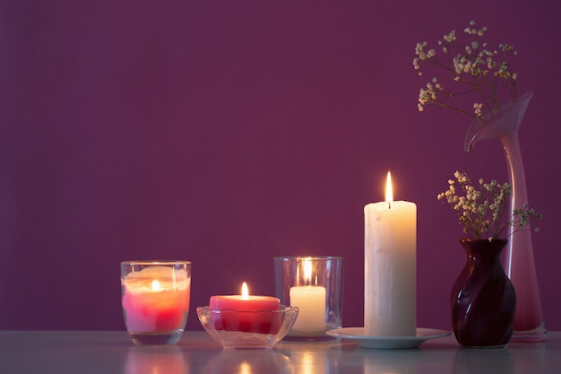 Velas com flores na mesa de madeira branca sobre fundo roxo