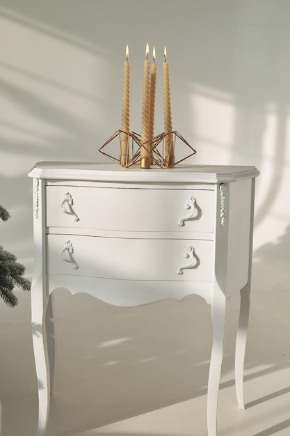 Velas de ouro de Natal acesas queimam em um castiçal na mesa de cabeceira em uma sala decorada com design de Ano Novo perto de abeto de árvore nevado artificial