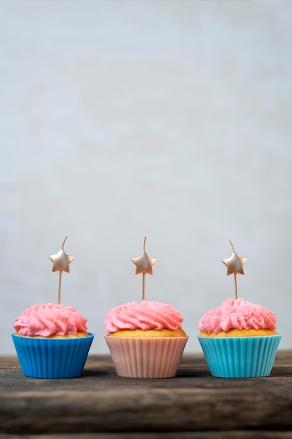Velas douradas em forma de estrela em cupcakes com cobertura de creme de manteiga rosa. Cupcakes de aniversário na mesa de madeira. Fundo cinza. Comida de festa. Moldura vertical