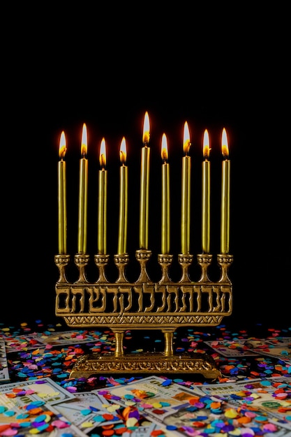 Velas douradas na menorá e confetes com dinheiro na superfície preta. Símbolo de Hanukkah feriado judaico.