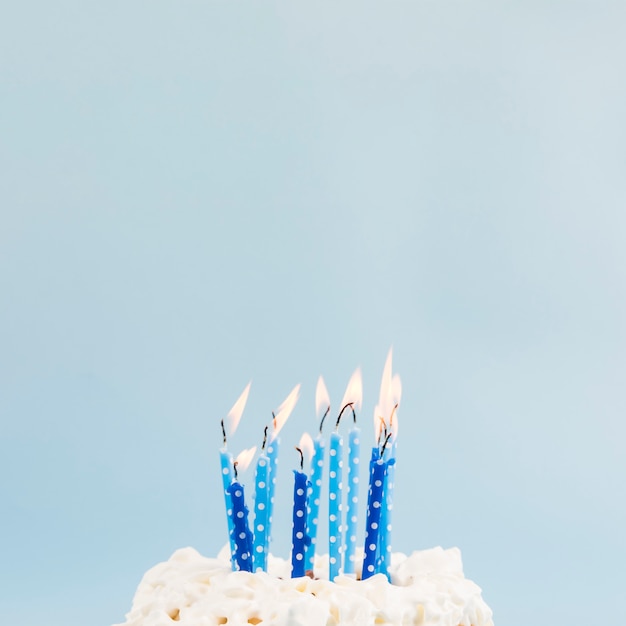 Foto velas encendidas azules sobre la torta de cumpleaños contra el fondo azul