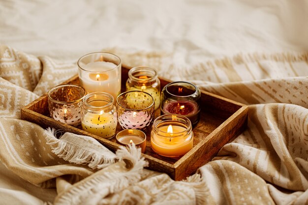 Velas encendidas en bandeja de madera con cuadros cálidos en la cama. Estilo escandinavo. Concepto Hygge.