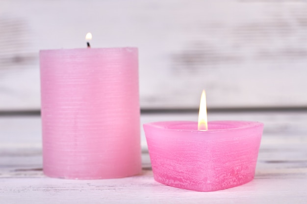 Velas encendidas de cera rosa sobre fondo blanco de madera.