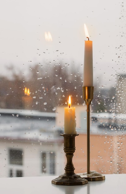 Velas encendidas en el cristal de la ventana de lluvia de fondo