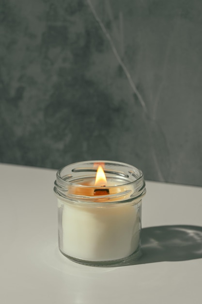 Velas encendidas en un frasco de vidrio en una superficie blanca con fondo gris
