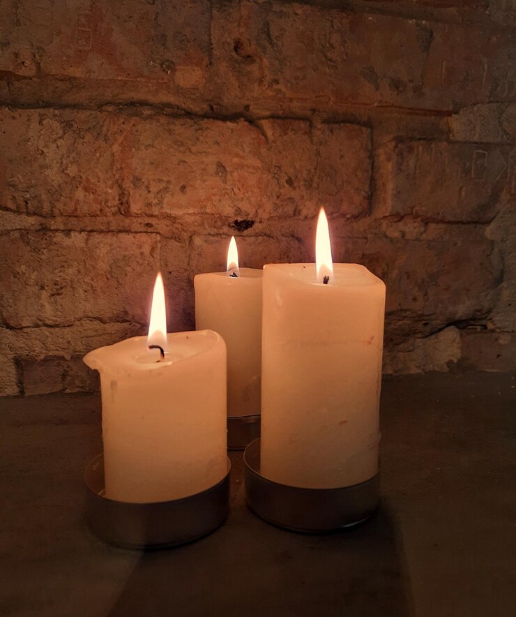 Velas encendidas en la pared de piedra. Hermosa composición con velas blancas en cuarto oscuro.