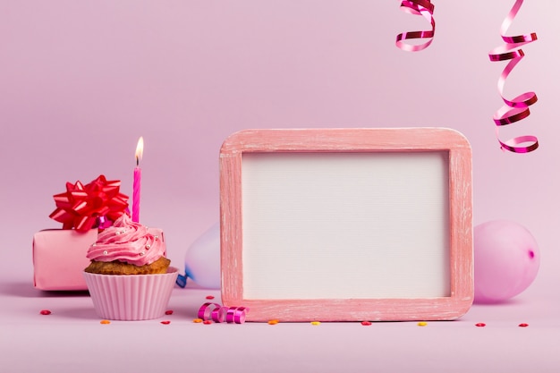 Foto velas encendidas sobre los muffins con pizarra de marco blanco sobre fondo rosa