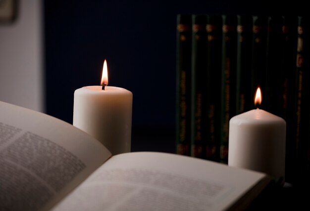 Velas con llama y libro de lectura sobre fondo negro de escritorio