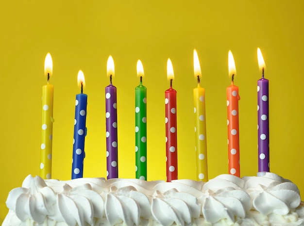 Velas multicolores arden en un pastel de cumpleaños sobre un fondo amarillo