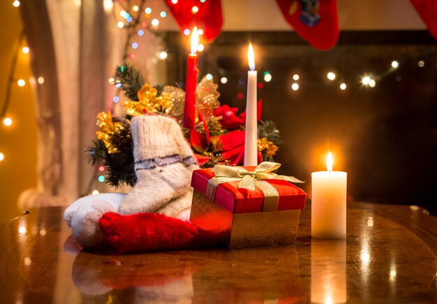 Velas de Navidad, caja de regalo y calcetín de lana colocado sobre la mesa contra la chimenea