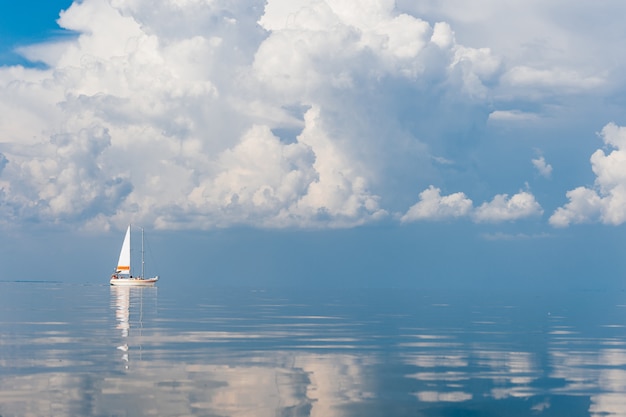 Foto velero en el mar en un día soleado en el fabuloso cuento de hadas pintoresco paisaje marino con nubes reflejadas en el agua.