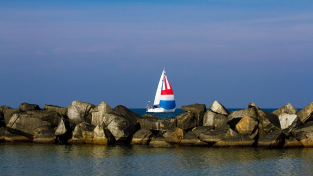Velero en el mar por las rocas contra el cielo