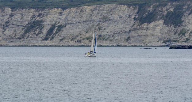 velero en mar tranquilo con acantilado en el fondo