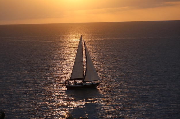 Velero moviéndose en el mar contra el cielo durante la puesta de sol