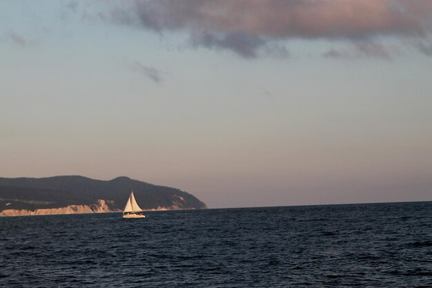 Un velero navega en el agua con una montaña al fondo.