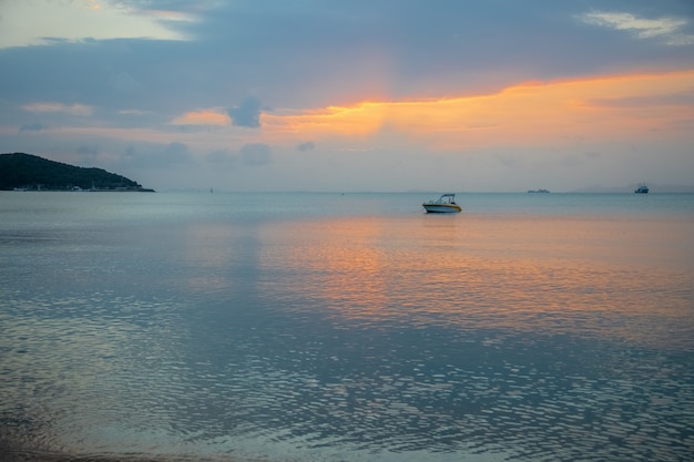 Un velero con puesta de sol brumosa y reflejo sobre el agua /
